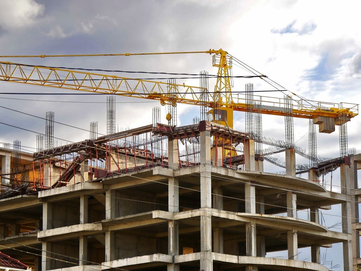 Construction site background. Construction crane near unfinished building under cloudy sky.