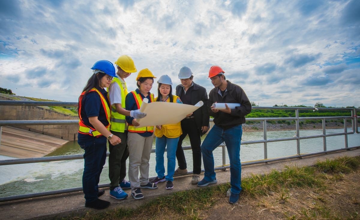 Six engineers are planning the construction, Team Engineers and supervisors are standing and reading the blueprint at the construction site, with blue sky background. - Image